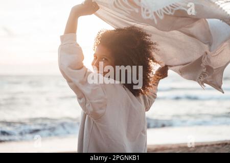 Fröhliche junge Frau mit Schal am Strand Stockfoto