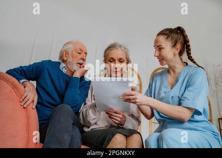 Lächelnde Krankenschwester, die Seniorinnen und Seniorinnen beim Lesen medizinischer Berichte zu Hause unterstützt Stockfoto