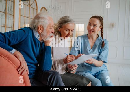Seniorin unterschreibt Dokument mit Mann und Pflegekraft zu Hause Stockfoto