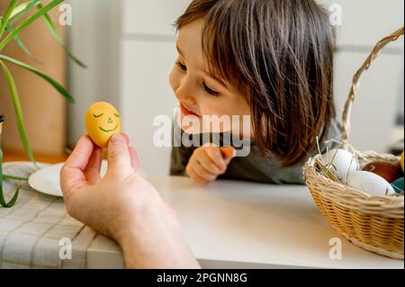 Ein lächelnder Junge, der zu Hause ein dekoriertes Osterei ansieht Stockfoto