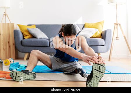 Junger Mann mit Behinderung, der sich vor dem Sport zu Hause aufwärmt Stockfoto