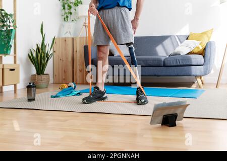 Junger Mann mit amputierter Beindehnung mit Widerstandsband zu Hause Stockfoto