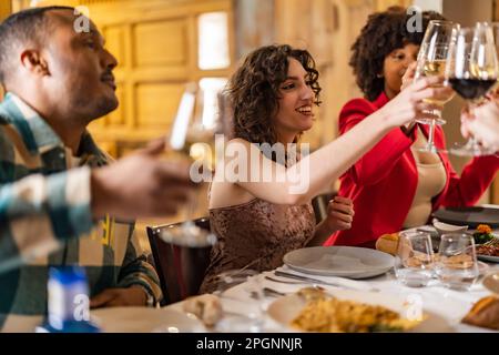 Glückliche Frauen, die mit Freunden auf der Dinnerparty auf Weingläser toasten Stockfoto