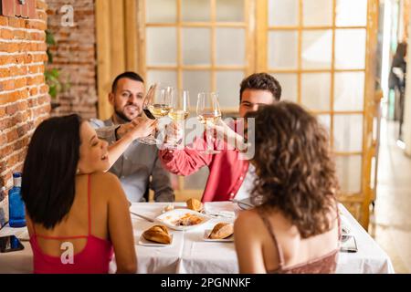 Junge Freunde, die im Restaurant auf Weingläser toasten Stockfoto