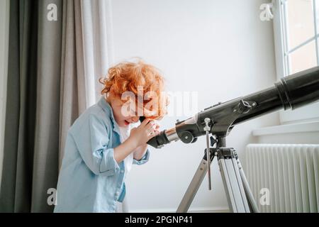 Neugieriger Junge, der zu Hause durch das Teleskop schaut Stockfoto