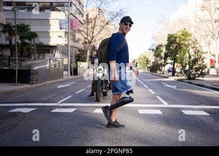 Lächelnder reifer Mann mit amputiertem Bein, der die Straße in der Stadt überquert Stockfoto
