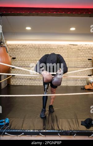 Reifer Mann mit Beinprothese, der im Boxring am Seil anlehnt Stockfoto