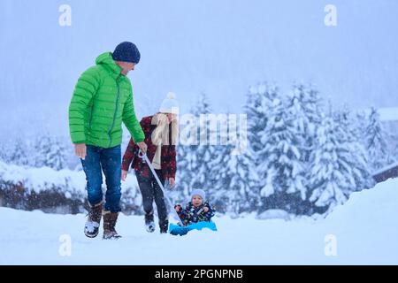 Mutter und Vater mit Sohn, der im Schnee auf einem Schlitten sitzt Stockfoto