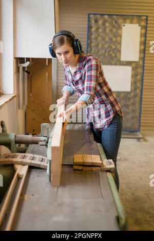 Handwerkerin mit Gehörschutz beim Holzschneiden in der Werkstatt Stockfoto