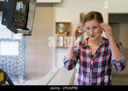 Lächelnde Zimmerlerin mit Schutzbrille in der Werkstatt Stockfoto