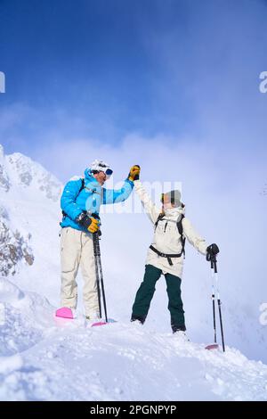 Ein Paar in Skikleidung gibt High-Five auf schneebedeckten Bergen Stockfoto