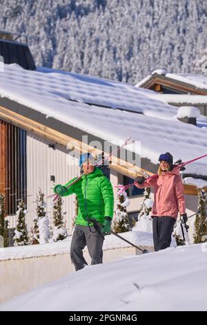 Mann und Frau mit Skiern, die vor dem Chalet laufen Stockfoto