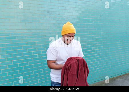 Glücklicher Mann mit rotem Hemd, der vor einer türkisfarbenen Wand steht Stockfoto