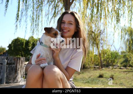 Glückliche junge Frau, die mit einem süßen Hund im Park sitzt Stockfoto