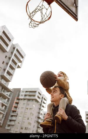 Vater trägt Tochter auf den Schultern und spielt Basketball Stockfoto