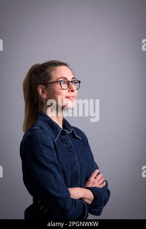 Eine durchdachte, reife Geschäftsfrau, die eine Brille vor grauem Hintergrund trägt Stockfoto
