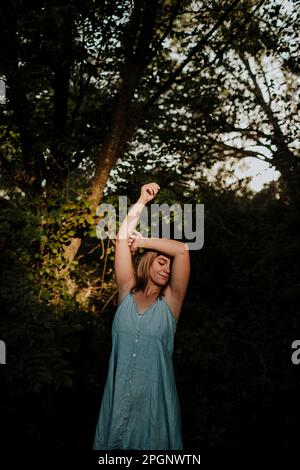 Junge Frau mit erhobenem Arm, die vor dem Baum steht Stockfoto