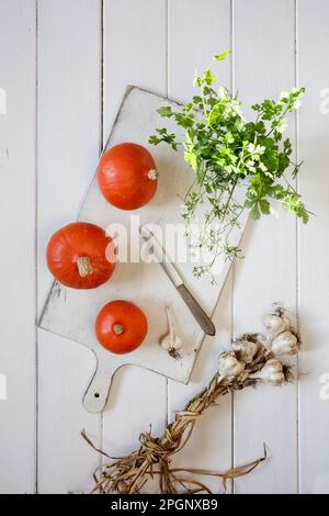 Rote Kuri Kürbisse, Knoblauch und Koriander liegen auf weißem Schneidebrett Stockfoto
