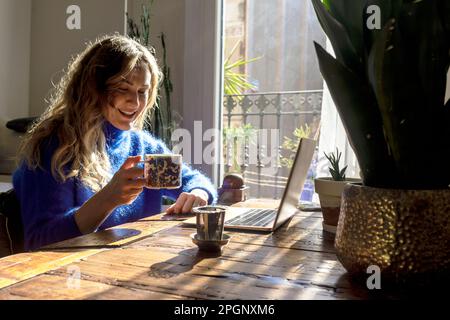 Frau, die zu Hause eine Tasse Tee hält und an einem Notebook arbeitet Stockfoto
