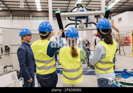 Ingenieure tragen Schutzhelm, um Maschinenteile in der Roboterfabrik zu untersuchen Stockfoto