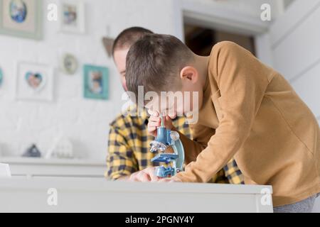 Ein neugieriger Junge, der durch das Mikroskop am Tisch schaut, von Vater zu Vater Stockfoto