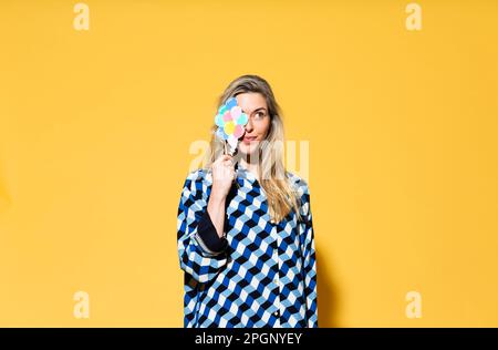 Lächelnde Frau, die das Auge mit Papierballon auf gelbem Hintergrund verdeckt Stockfoto