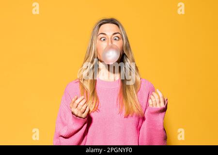 Eine Frau, die Kaugummi vor gelbem Hintergrund kaut Stockfoto