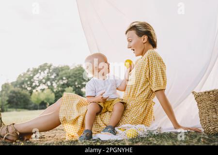 Ein lächelnder Junge, der seiner Mutter im Park Früchte gibt Stockfoto