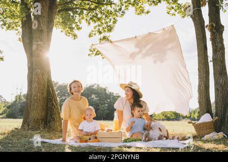 Glückliche Frauen, die mit Söhnen auf einer Picknickdecke im Park sitzen Stockfoto