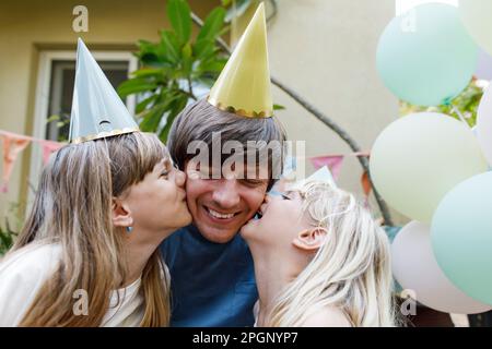 Töchter küssen glücklichen Vater auf die Wangen im Garten Stockfoto