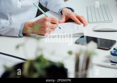 Hand des Arztes, der am Schreibtisch ein Rezept mit Stift schreibt Stockfoto