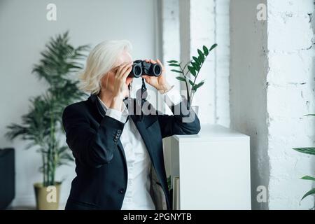 Reife Geschäftsfrau, die durch ein Fernglas schaut Stockfoto