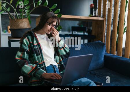 Müder junger Student, der zu Hause mit einem Laptop auf dem Sofa sitzt Stockfoto