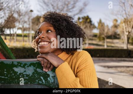 Aufmerksam lächelnde junge Frau, die sich auf der Rutsche auf dem Spielplatz lehnt Stockfoto