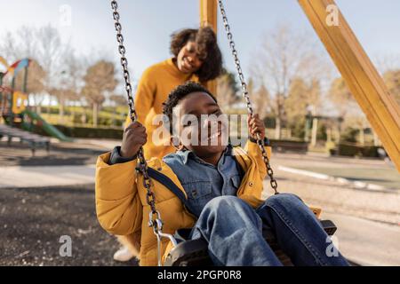 Fröhliche Mutter, die den Sohn auf dem Spielplatz schubst Stockfoto