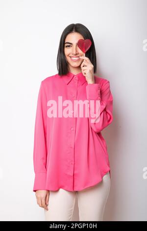 Glückliche junge Frau mit herzförmigem Lutscher vor weißem Hintergrund Stockfoto