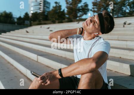 Junger Mann, der sich den Hals streckt und auf Treppen sitzt Stockfoto