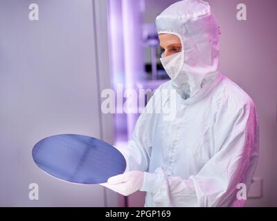 Ingenieur trägt Schutzanzug und hält Wafer-Chip im Labor Stockfoto