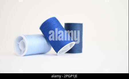 Drei Spulen blaues Garn in verschiedenen Schattierungen auf weißem Hintergrund Stockfoto