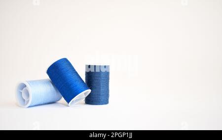 Drei Spulen blaues Garn in verschiedenen Schattierungen auf weißem Hintergrund. Speicherplatz kopieren Stockfoto