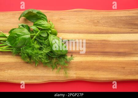 Holzbrett mit frischen Kräutern auf rotem Hintergrund, Nahaufnahme Stockfoto