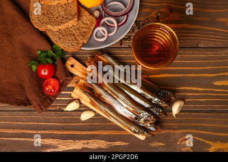 Gehen Sie an Bord mit köstlicher geräucherter Lodde, einem Glas Bier und einem Teller mit Snacks auf Holzhintergrund Stockfoto