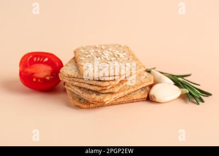 Ein Stapel leckerer Cracker mit Sesam, Knoblauch, Tomaten und Rosmarin auf beigefarbenem Hintergrund Stockfoto