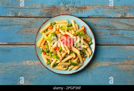 Teller mit leckerem Nudelsalat auf blauem Holzhintergrund Stockfoto