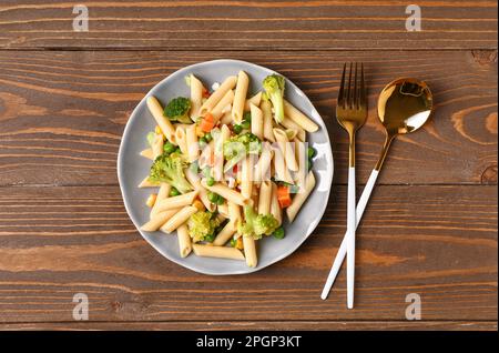 Teller mit leckerem Nudelsalat auf Holzhintergrund Stockfoto