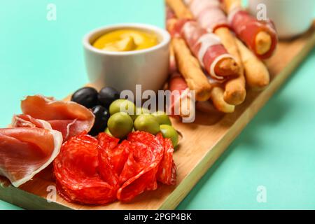 Holzbrett mit Speck, Würstchen und Oliven auf türkisfarbenem Hintergrund, Nahaufnahme Stockfoto