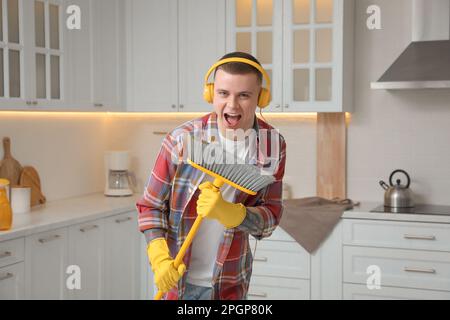 Ein hübscher junger Mann mit Kopfhörern, der beim Putzen der Küche singt Stockfoto