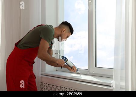 Bauarbeiter versiegelt Fenster mit Versiegelung in Innenräumen Stockfoto