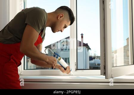 Bauarbeiter versiegelt Fenster mit Versiegelung in Innenräumen Stockfoto