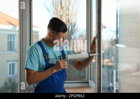 Bauarbeiter versiegelt Fenster mit Versiegelung in Innenräumen Stockfoto